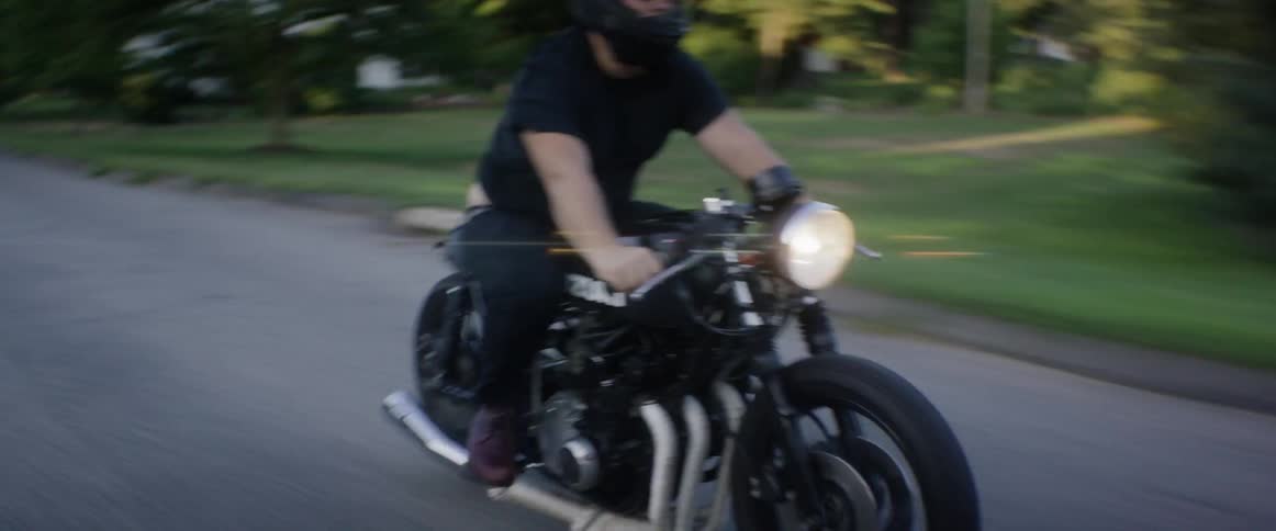 A man on a motorcycle speeds along a narrow road with houses