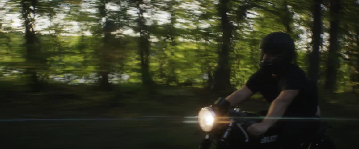 A man rides a motorcycle on a tree lined road