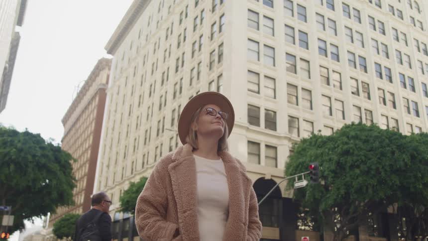 Woman wearing a hat and jacket stands on the city street looking up