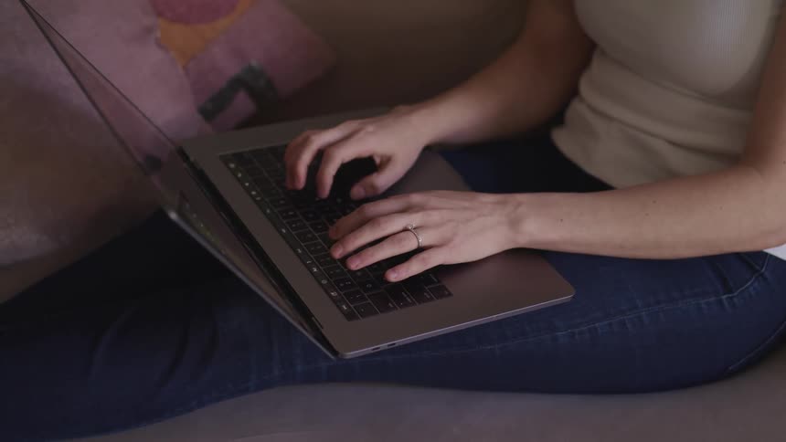 A woman types on a laptop while sitting on a sofa