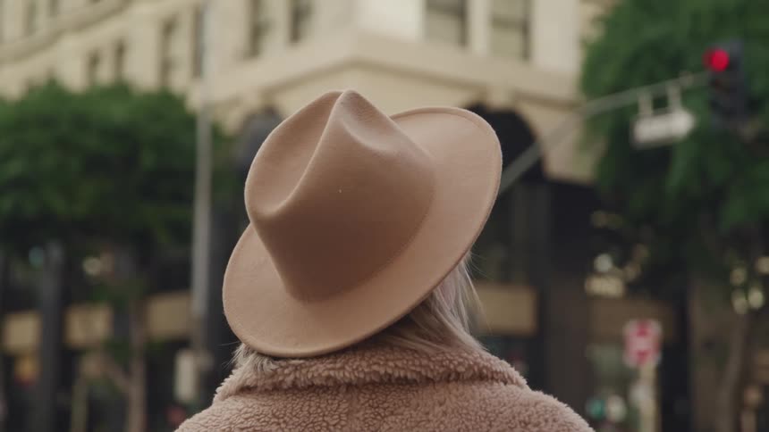 Woman with a brown hat and an overcoat looks up at buildings in the city