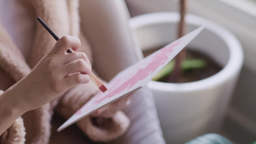 A young female applies delicate brush strokes to a small water color painting