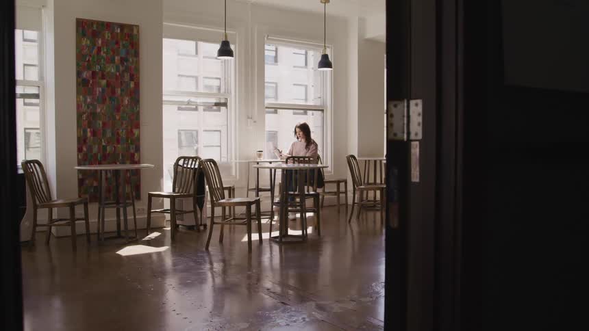 A woman looks at her phone as she sits in a quiet cafe with a coffee