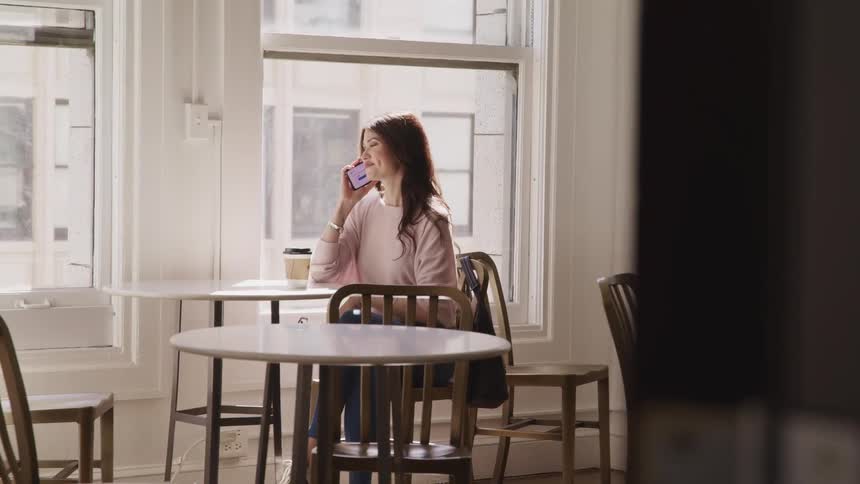 Young woman ends a call on her smartphone while sitting at a table in a cafe