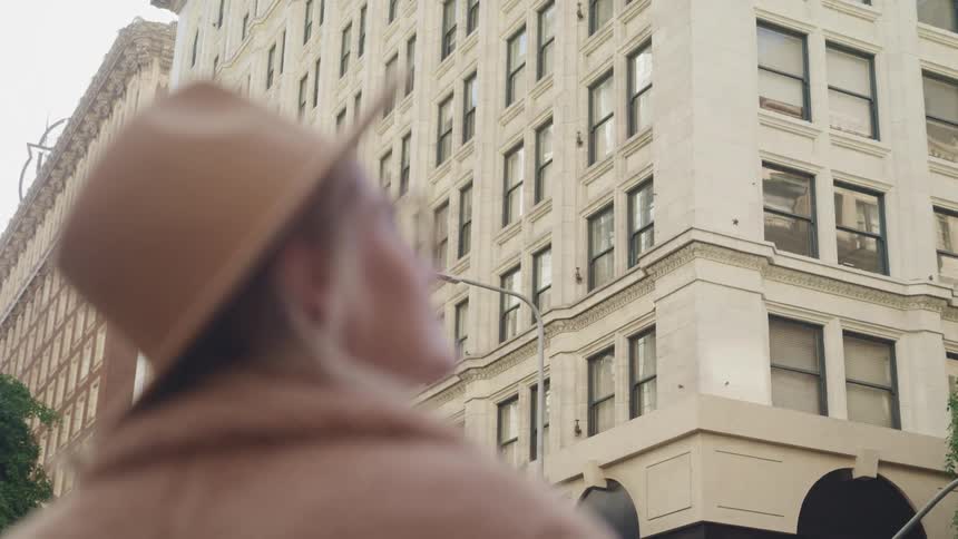 Woman stands looking up at mid rise buildings under light sky