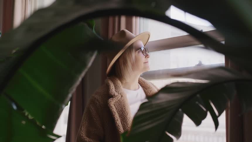 A woman at home looks out the window and smiles