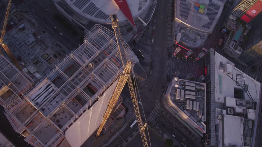 A construction crane next to an unfinished building surrounded by streets and vehicles