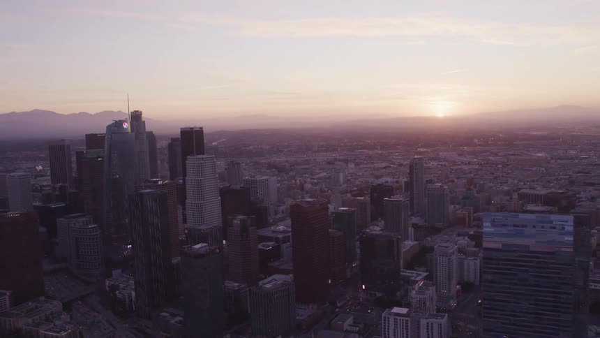 Aerial view of citys downtown skyscrapers while the sun sets over the mountains