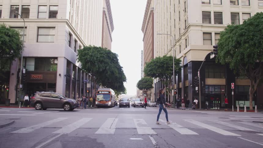 A woman walks across a large city cross walk at an intersection with vehicles passing by