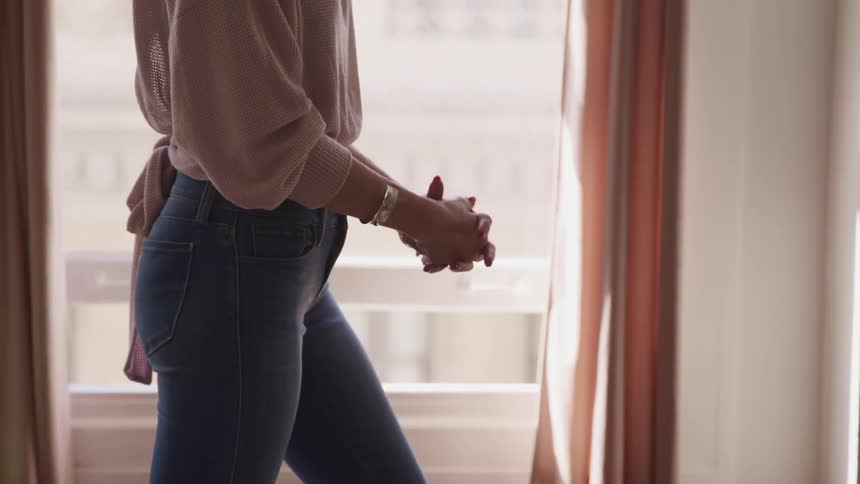 A young woman stands in front of window while fidgeting her hands