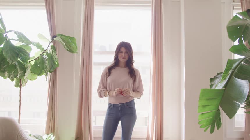 Woman stands in front of window in living room smiling