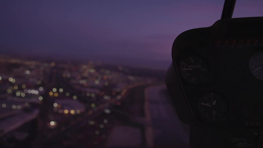 Dashboard of a helicopter flying over the city lights at sunset