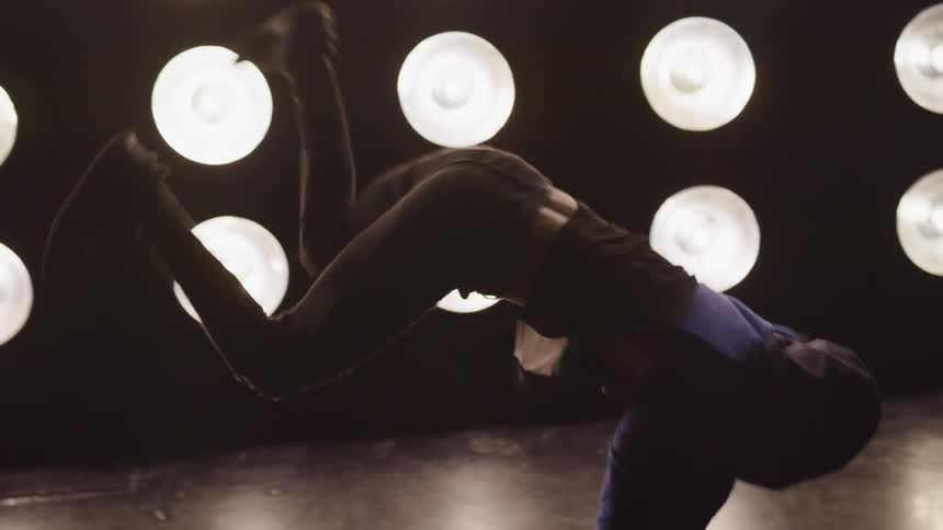 Young man break dances on the floor in front of flood lights in a stage