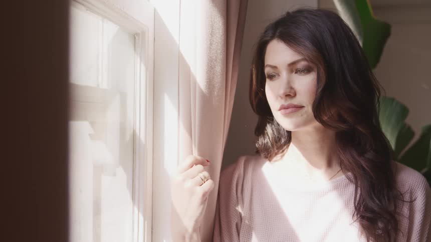Woman looks out the window and smiles as the sunlight streams in