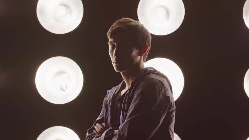 Man wearing hoodie stands with arms crossed in front of columns of large lights hung against a black background