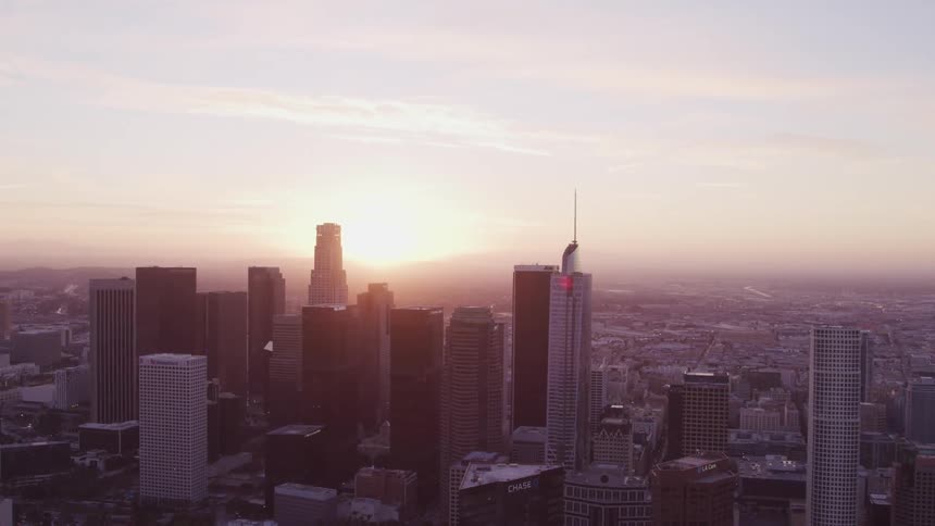 Skyscrapers loom over a metropolis as the sun peaks over the horizon