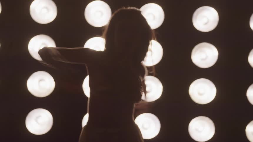 A young woman dances in front of an array of stage lights