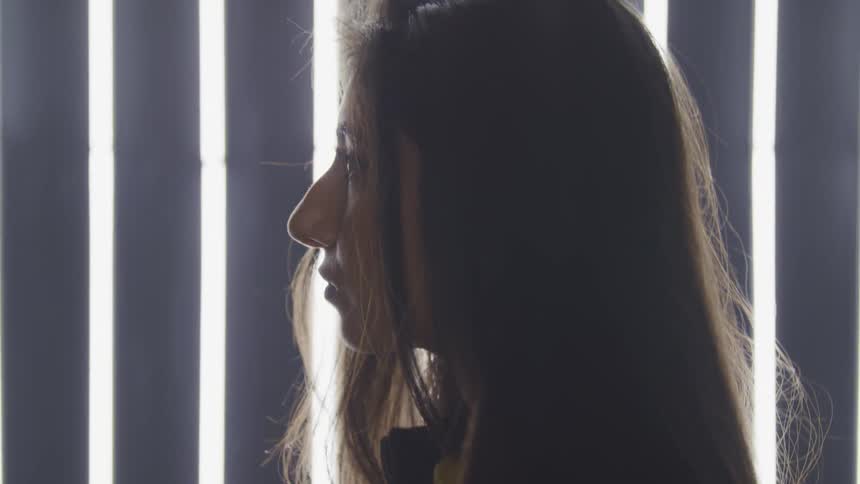 A young woman standing in front of bright lights raises her head