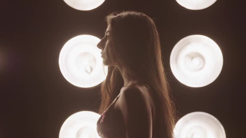 Woman lifts her head as she stands in front of the bright lights