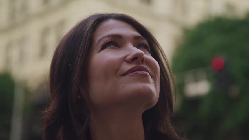 Woman stands in a city and looks up at something above