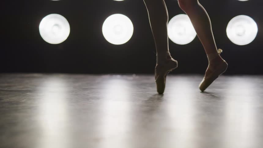 A ballerina dances en pointe on a stage with spotlights