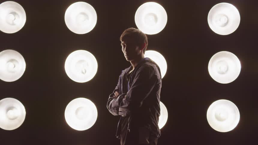 A man stands with arms crossed in front of rows of glowing lights