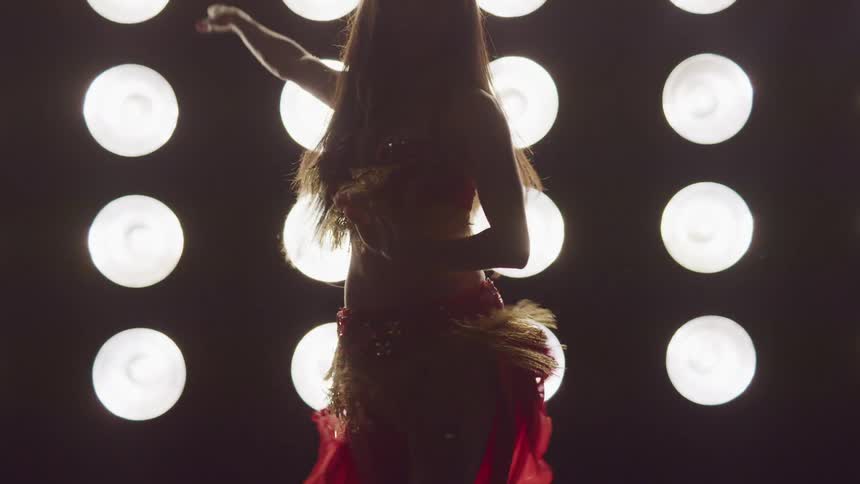 A woman is belly dancing in front of lights