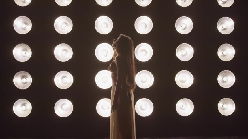A woman standing in front of bright lights lifts her head and looks up