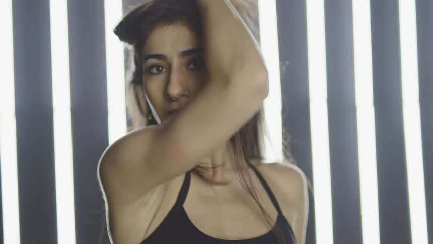 A woman dances and spins in front of a wall with vertical lights