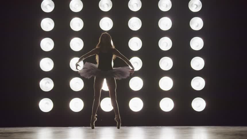 A ballerina dances on a stage lit with with circular lights lined in columns