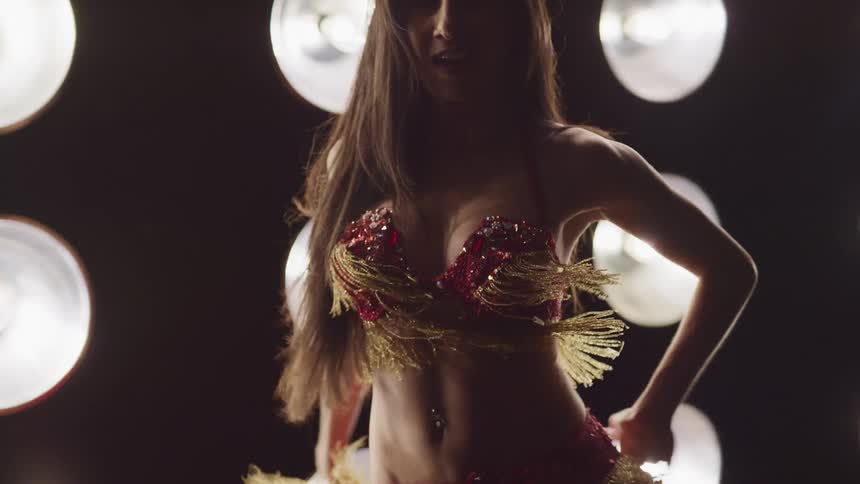 Belly dancer with long brown hair performs a dance moving her hips and stomach