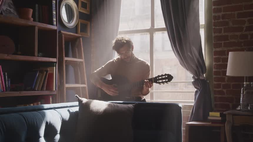 Man sits in living room near window in sunlight playing guitar