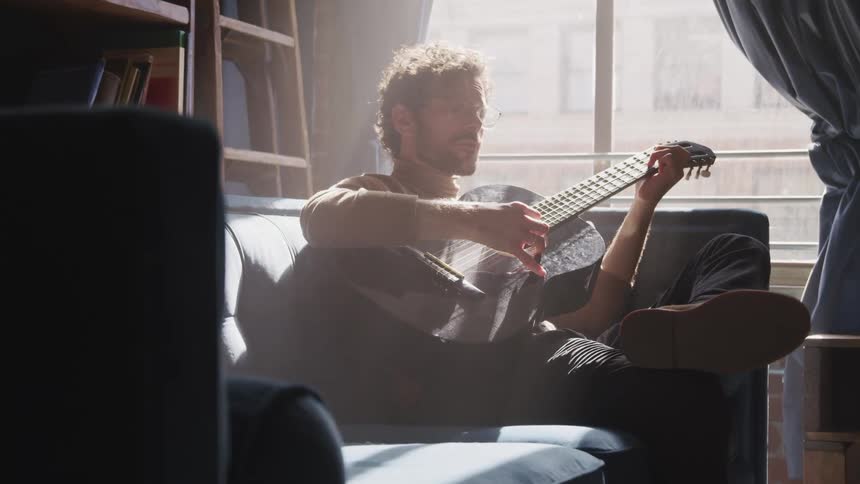 A man is sitting on a couch and playing guitar