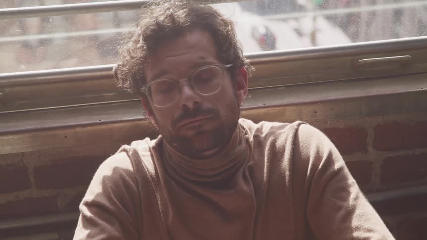 A man rests with his eyes closed against a wall beneath a window