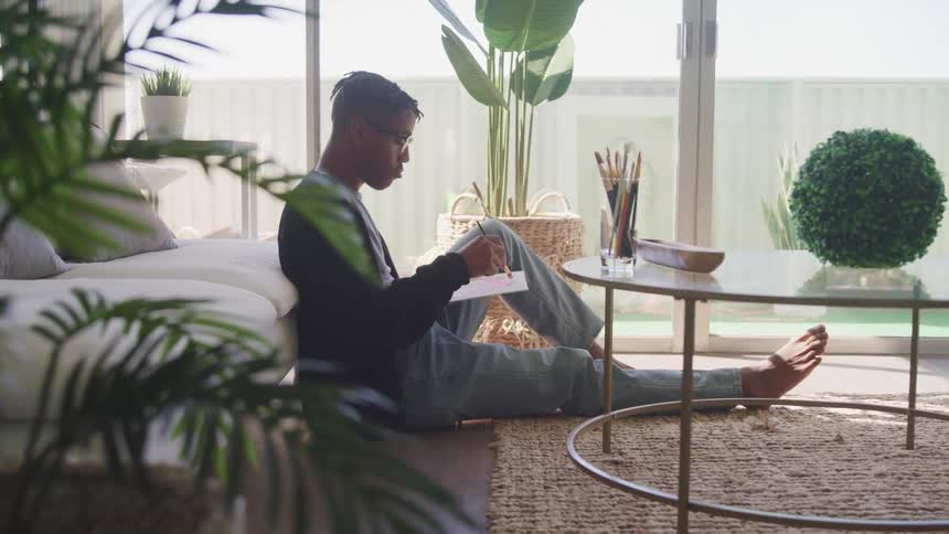 Young man sitting over the rug in the living room paints over a small canvas