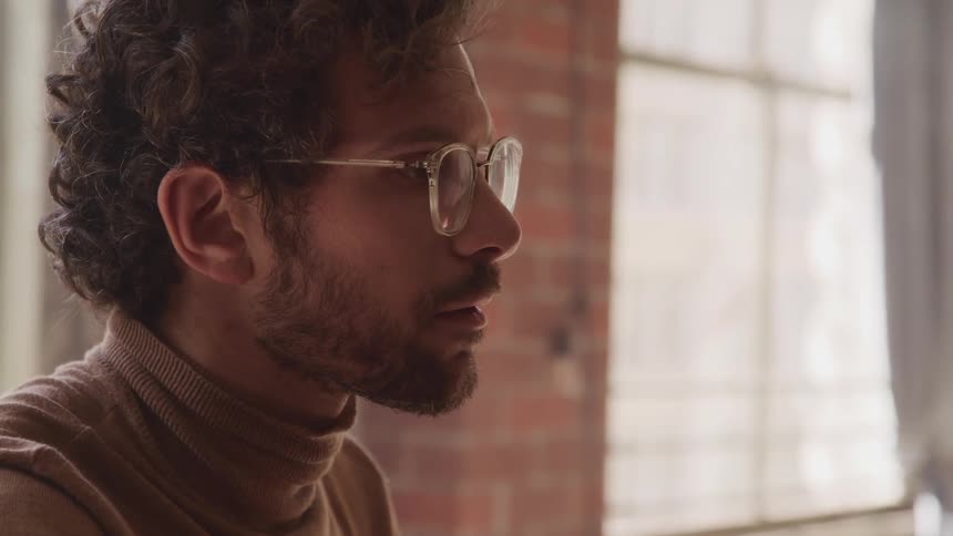 Side view of a man with a brown turtleneck sweater a beard and glasses