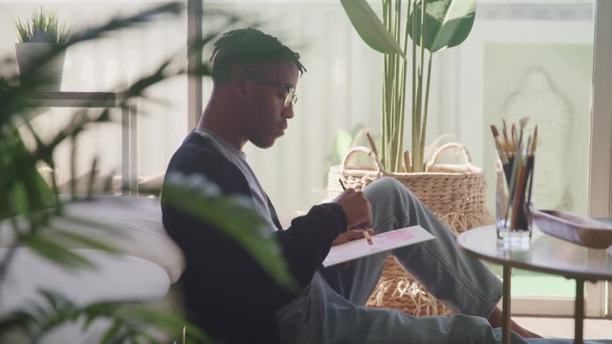 A man sits on the floor in front of his couch and paints
