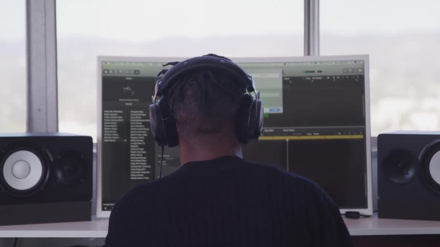 Man wearing headphones sits in front of a computer editing and mixing audio