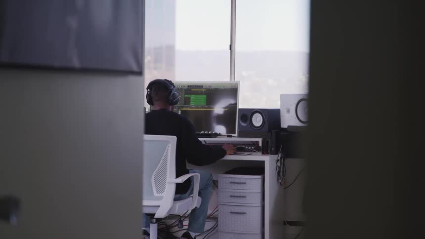 Black man sits at a desk uses a computer with speakers in studio