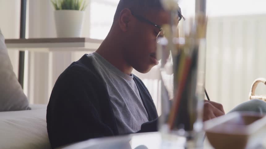 Artist sits in room near houseplants and art supplies drawing