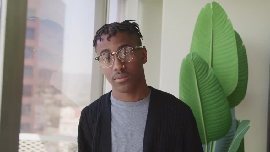 A young black man turns his head away from the window to look into the camera