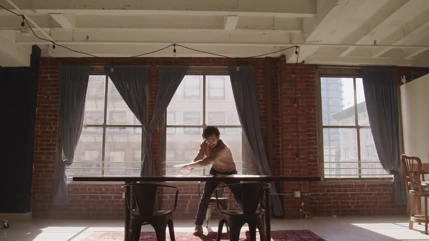 A man with glasses and holding a pencil throwing paper off of a table