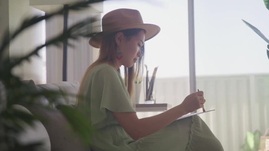 Young woman sitting in a couch paints with a brush over cardboard