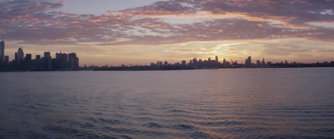 The sun sets over a cityscape with a rippling body of water in the foreground