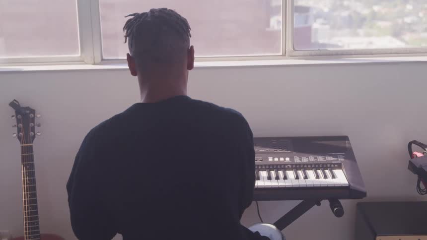 A man sits in front of a electronic keyboard in a room filled with musical equipment