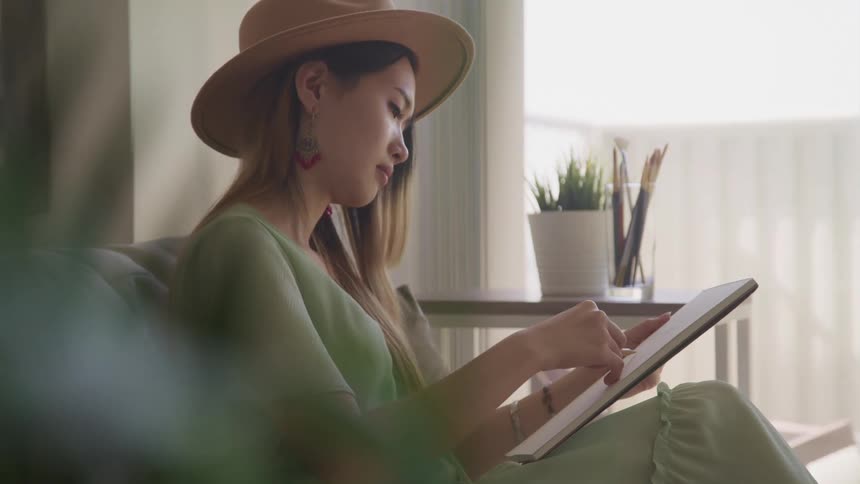 A woman sits on a couch sketching in a sketch book
