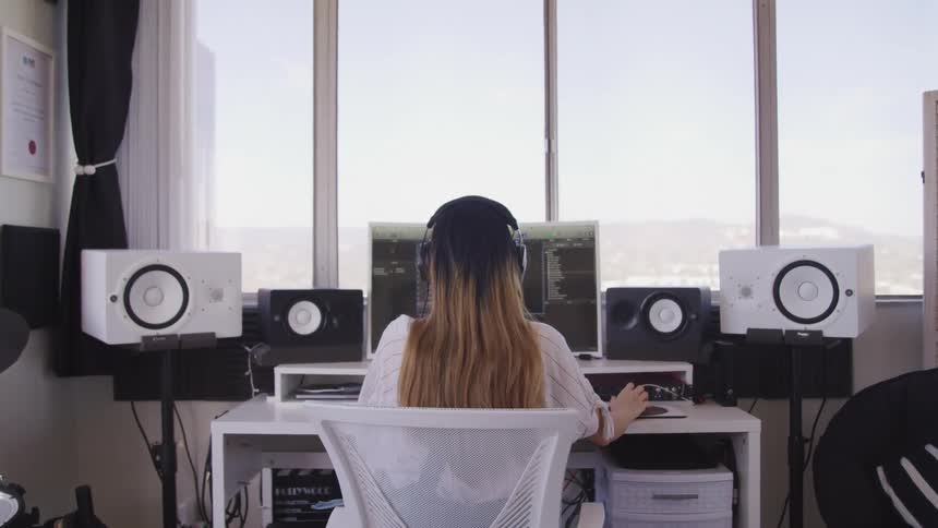Woman sits in front of a computer surrounded by speakers in her office