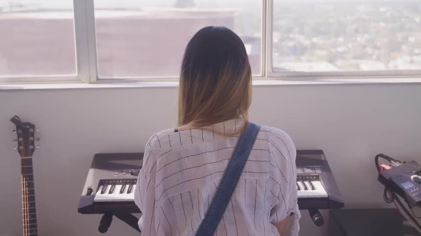 A woman sits at a keyboard facing a large window outside