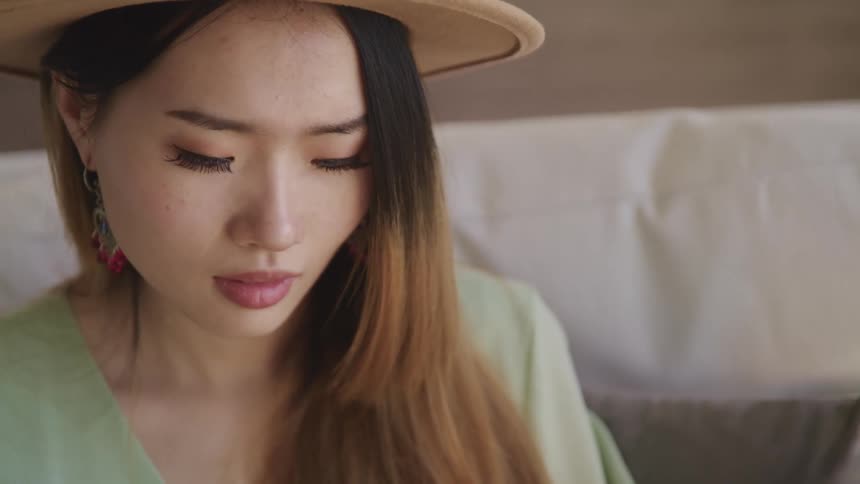 Asian woman with brown hat earrings and makeup looks around