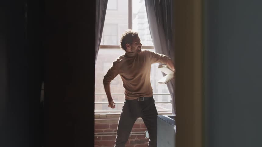 Man with a brown turtleneck sweater holds a book and tears up a page and throws it away